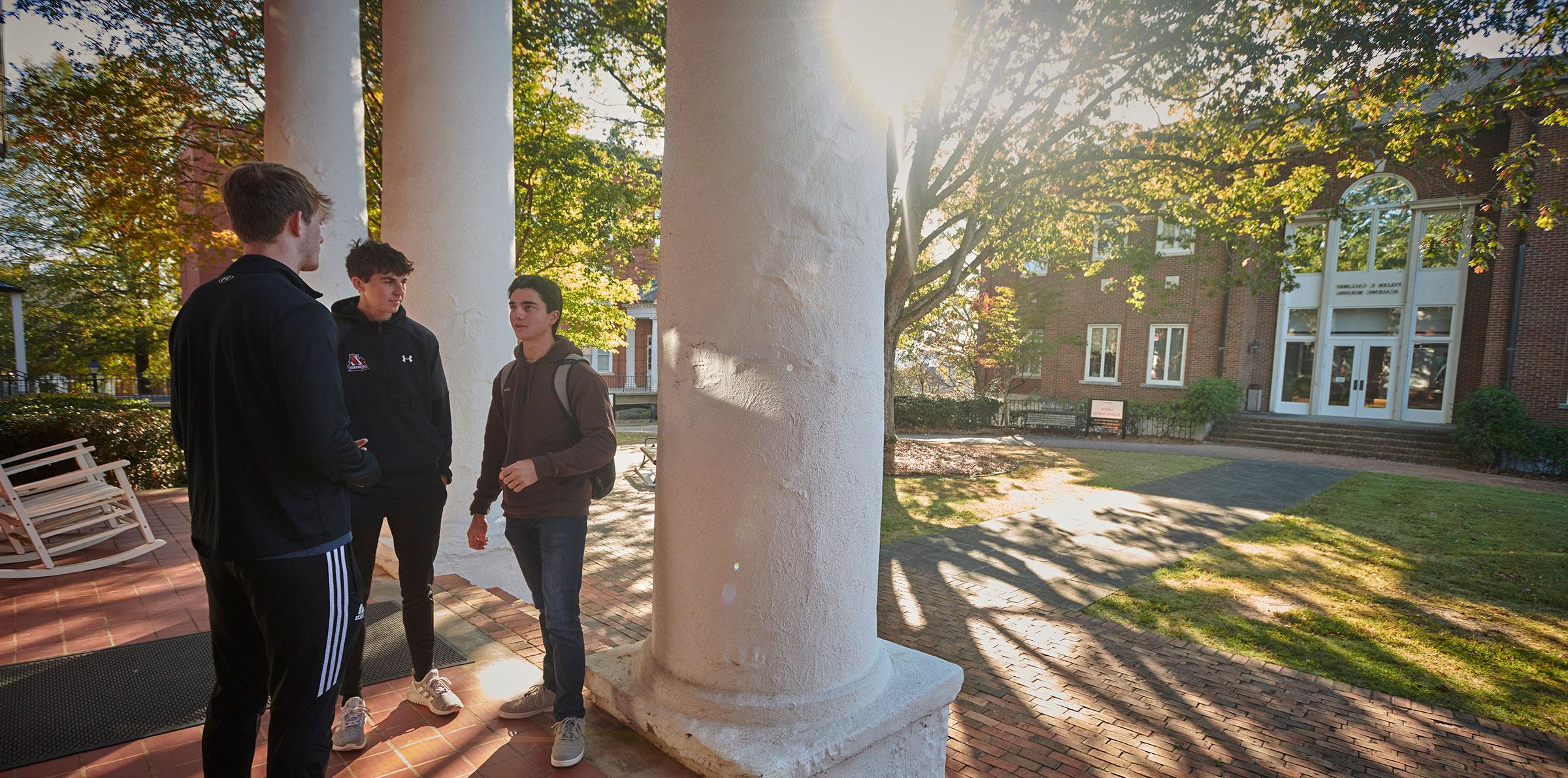 Three male college students standing in front of Smith Hall